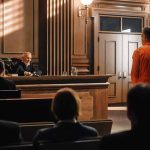 Courtroom scene with judge and defendant in orange jumpsuit.