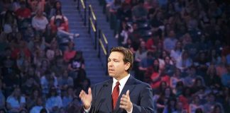 Person speaking on stage with a large audience behind.