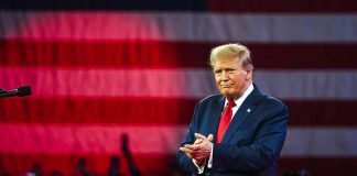 Man clapping on stage with flag background.