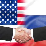 Hands shaking in front of USA and Russia flags.