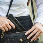 Person placing gun into a handbag.