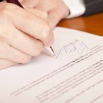 Hand signing a document on wooden desk