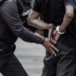 Police arresting person against a wall outdoors