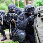 SWAT team members aiming rifles behind a protective shield.