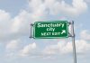 Green road sign saying sanctuary city next exit