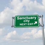 Green road sign saying sanctuary city next exit