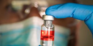 Gloved hand holding vial with red liquid and flag