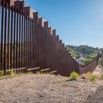 Tall metal border wall with rural landscape