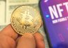 Person holding Bitcoin coin NFT text on screen