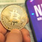 Person holding Bitcoin coin NFT text on screen
