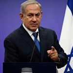 Man in suit giving speech in front of Israeli flag