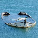 Half-submerged, weathered, abandoned boat floating on calm water.
