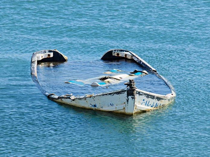 20081782 featured image Half-submerged, weathered, abandoned boat floating on calm water.