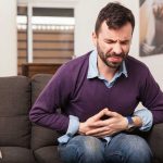Man sitting on couch holding stomach in pain
