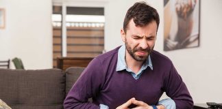 Man sitting on couch holding stomach in pain