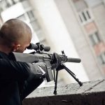 Person aiming a rifle from a building balcony