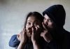 Man holding woman's mouth, gesturing silence