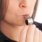 Person blowing a silver whistle close up