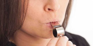 Person blowing a silver whistle close up