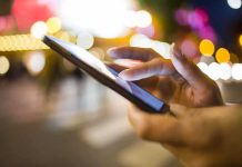A persons hand using a smartphone in a city at night with blurred lights in the background