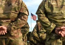 Soldiers stand in formation with American flag in background.