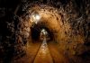 Dimly lit underground tunnel with rail tracks and rocky walls