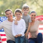 A family of four posing outdoors with an American flag