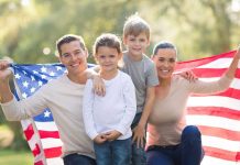 A family of four posing outdoors with an American flag