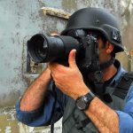 A photographer in military gear aiming a camera