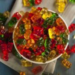 A bowl filled with colorful gummy bears surrounded by scattered candies