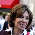 A smiling woman engaging with a crowd at a political event