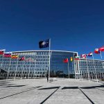 Flags outside NATO headquarters building under clear blue sky