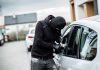 Person in black breaking into a car.
