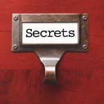 A label holder on a wooden surface with the word Secrets displayed
