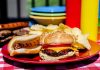 A plate with a hamburger, hot dog, and potato chips on a picnic table
