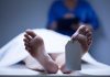 A deceased body on a table with a tag on the foot, and a medical professional in the background