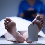 A deceased body on a table with a tag on the foot, and a medical professional in the background