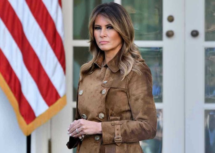 Woman in brown coat beside American flag