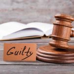 A wooden gavel next to a card that reads Guilty and an open book