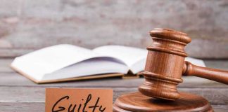 A wooden gavel next to a card that reads Guilty and an open book