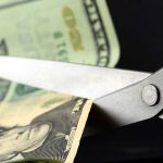 Scissors cutting a dollar bill against a dark background