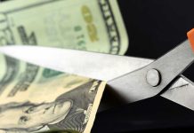 Scissors cutting a dollar bill against a dark background