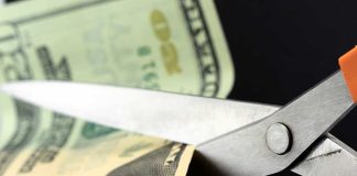 Trump CUTS $28 Billion During Standoff Scissors cutting a dollar bill against a dark background