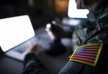 AI-Driven Combat: Could It Backfire? Soldier using laptop with US flag patch visible.