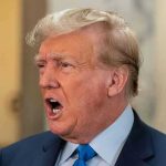 Man in suit with open mouth, speaking passionately.