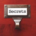 Metal label holder saying Secrets on wood background