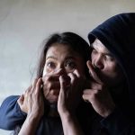 Man holding womans mouth, gesturing silence.