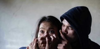 Man holding womans mouth, gesturing silence.