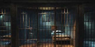 Empty prison cell with metal bars and bed.