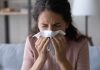 Hospital Chiefs Brace — 2025 Flu Outlook Darkens Woman sneezing into a tissue indoors.